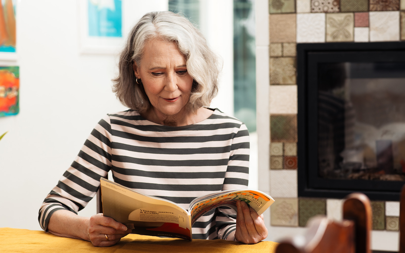Vanhempi nainen lukee aikakauslehteä keittiönpöydän ääressä.